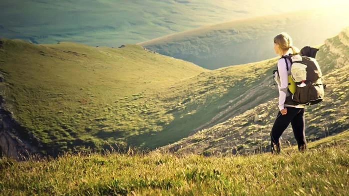 a person with a backpack walking on a grassy hill