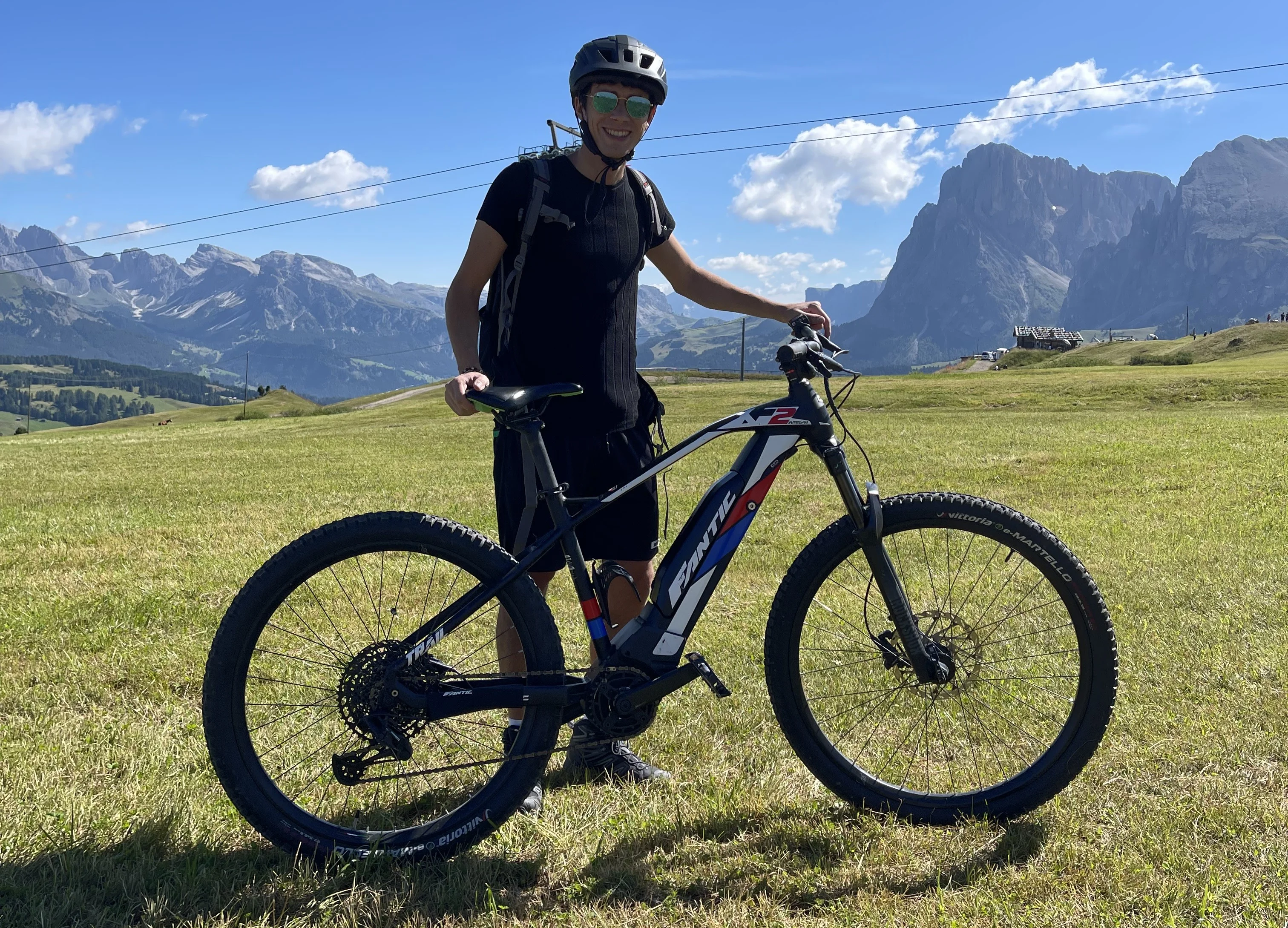 a man on a bicycle in a grassy field with mountains in the background